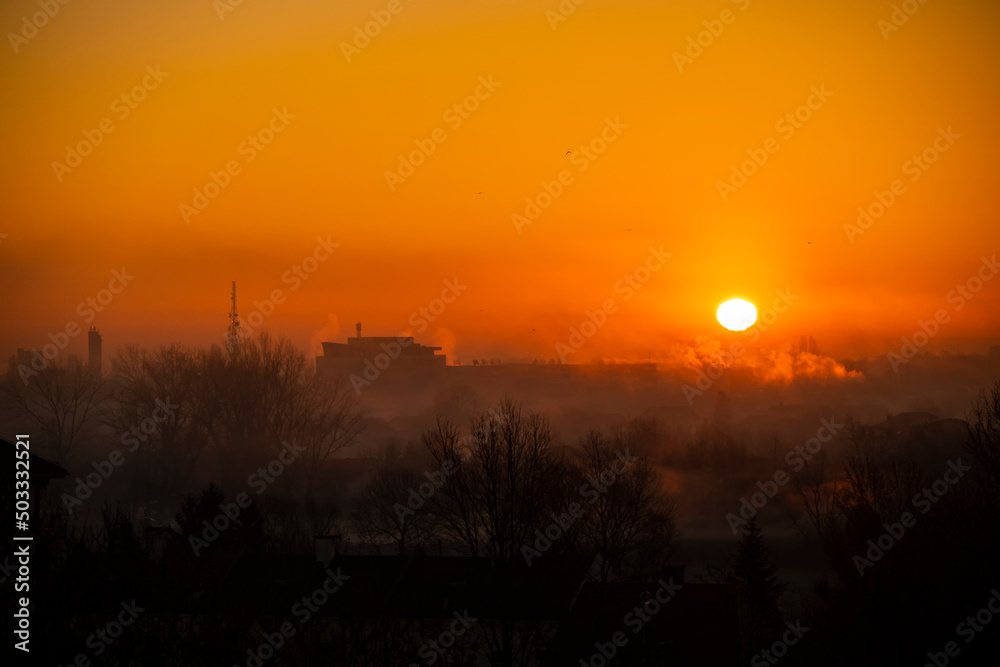 Wonderful, misty morning with sun painting sky orange, creating silhouettes of trees and buildings covered in mist