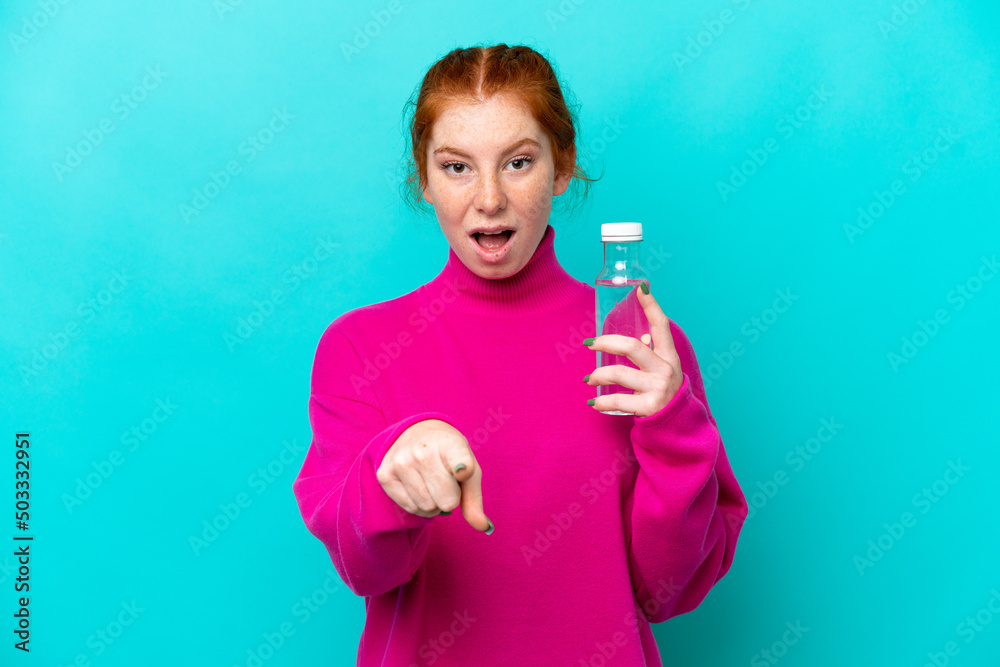 Young caucasian reddish woman with a bottle of water isolated on blue background surprised and pointing front Young caucasian reddish woman with a bottle of water isolated on blue background surprised and pointing front