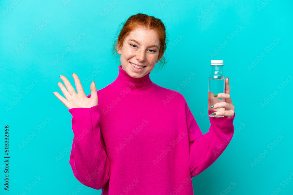 Young caucasian reddish woman with a bottle of water isolated on blue background saluting with hand with happy expression Young caucasian reddish woman with a bottle of water isolated on blue background saluting with hand with happy expression