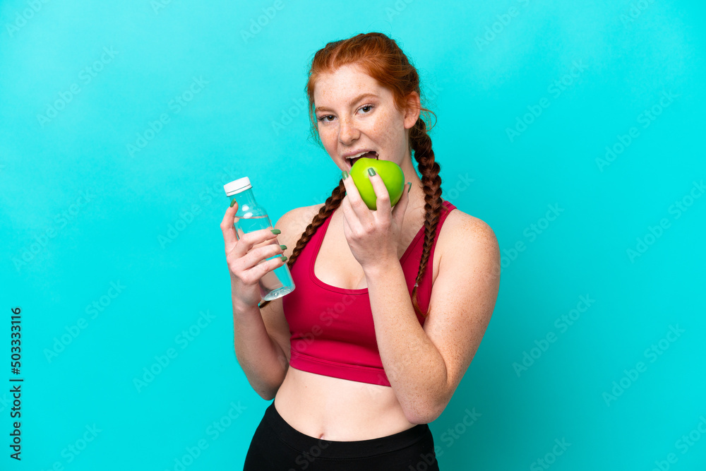 Young reddish woman isolated on blue background with an apple and with a bottle of water Young reddish woman isolated on blue background with an apple and with a bottle of water