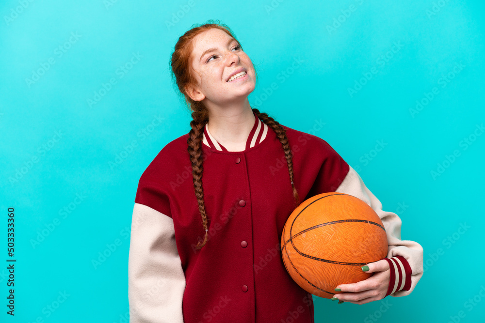 Young reddish woman playing basketball isolated on blue background laughing