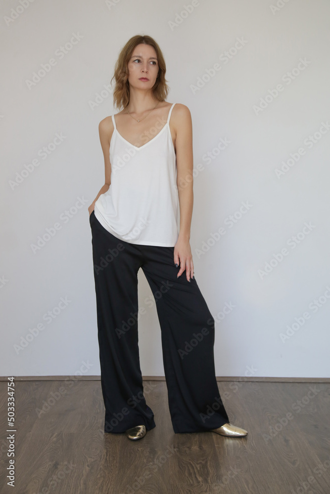 Female model wearing white camisole cotton top and black trousers. Classic and simple summer fashion. Studio shot. Female model wearing white camisole cotton top and black trousers. Classic and simple summer fashion. Studio shot.