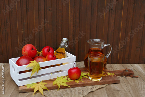 Krug und Glas mit Apfelsaft vor einer Holzwand.