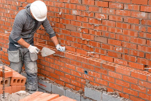 Bricklayer laying bricks on mortar on new residential house construction photo