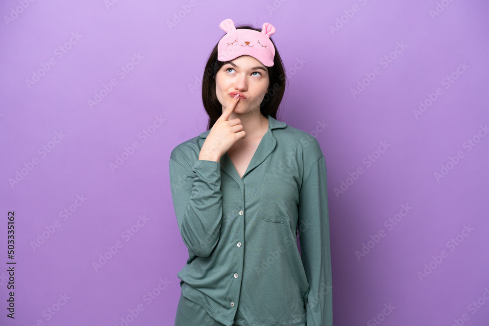 Young Russian woman in pajamas isolated on purple background having doubts while looking up Young Russian woman in pajamas isolated on purple background having doubts while looking up