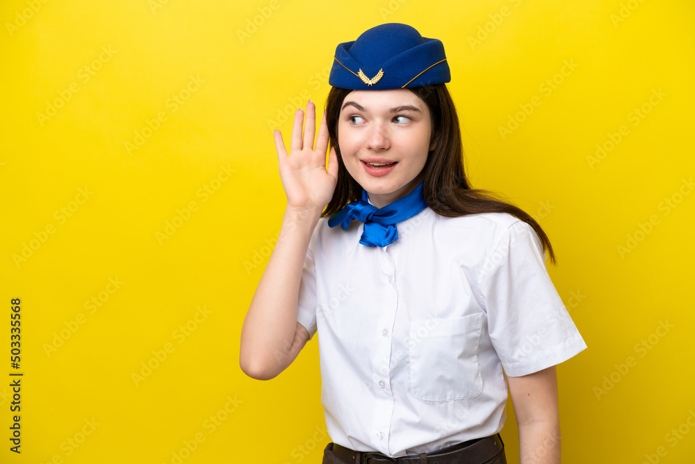 Airplane stewardess Russian woman isolated on yellow background listening to something by putting hand on the ear Airplane stewardess Russian woman isolated on yellow background listening to something by putting hand on the ear
