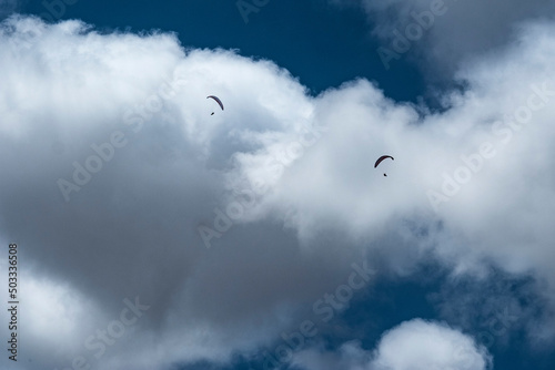 Two paragliders fly in front of a cloud 