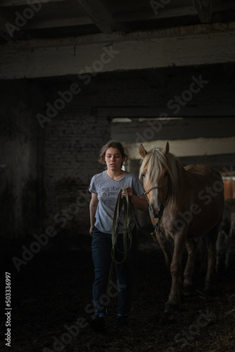 Картината върху платно A young beautiful female worker takes care of a horse on a farm.