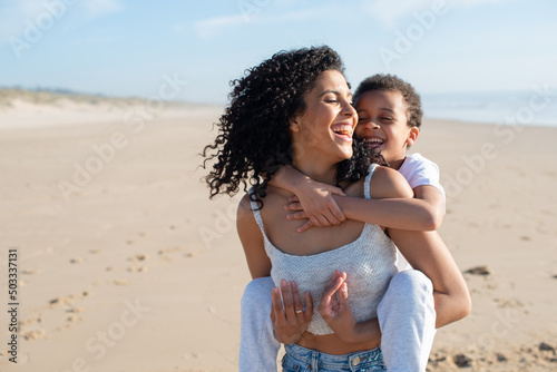 Joyful mother and son spending time on beach. African American family walking, laughing, playing, riding on back. Leisure, family time, parenthood concept