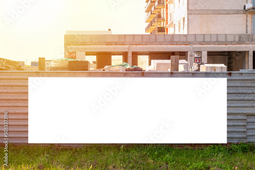 Blank white advertising billboard on the fence of construction site. Sunny summer evening. photo