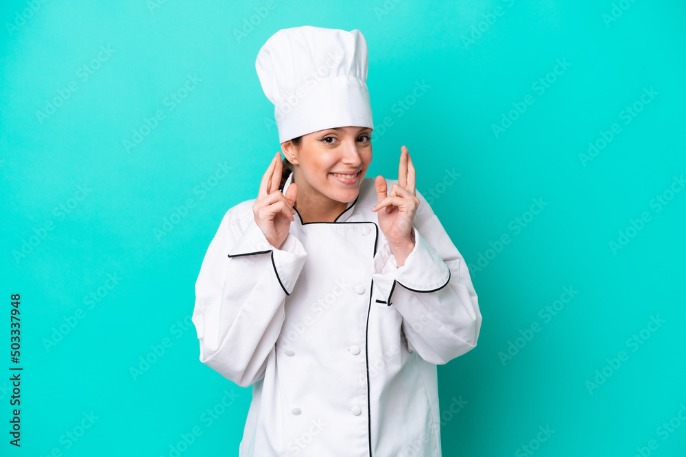 Young caucasian chef woman isolated on blue background with fingers crossing Young caucasian chef woman isolated on blue background with fingers crossing