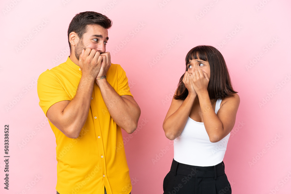 Young couple isolated on pink background is a little bit nervous and scared putting hands to mouth Young couple isolated on pink background is a little bit nervous and scared putting hands to mouth