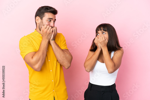 Young couple isolated on pink background is a little bit nervous and scared putting hands to mouth