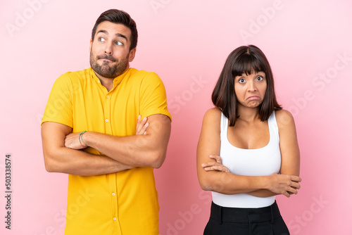 Young couple isolated on pink background making doubts gesture while lifting the shoulders
