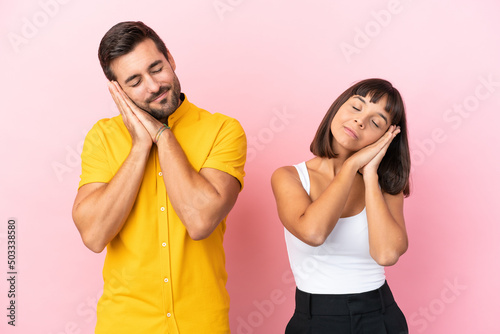 Young couple isolated on pink background making sleep gesture in dorable expression