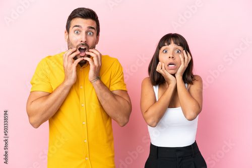 Young couple isolated on pink background surprised and shocked while looking right