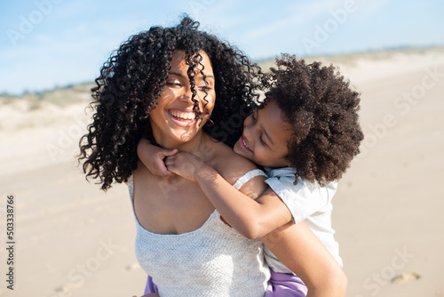 Tender mother and daughter spending time on beach. African American family walking, laughing, playing, riding on back. Leisure, family time, parenthood concept