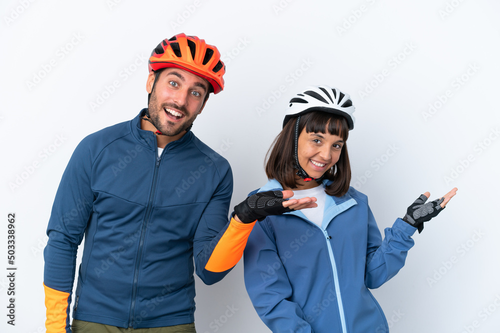 Young cyclist couple isolated on white background pointing back and presenting a product Young cyclist couple isolated on white background pointing back and presenting a product