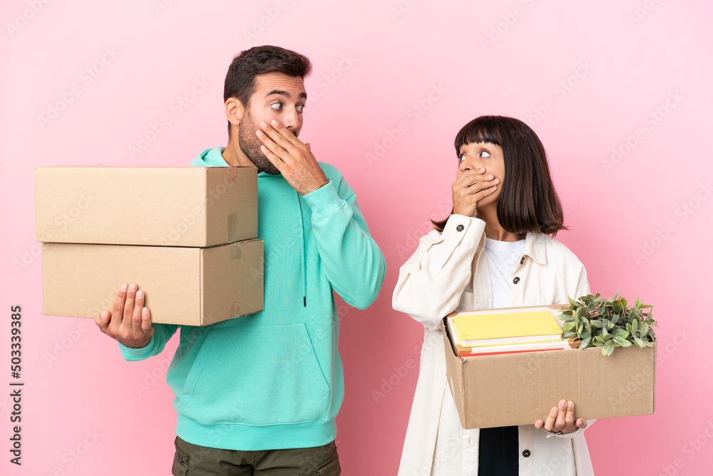 young beauty couple moving in new home among boxes isolated on pink background covering mouth with hands for saying something inappropriate young beauty couple moving in new home among boxes isolated on pink background covering mouth with hands for saying something inappropriate