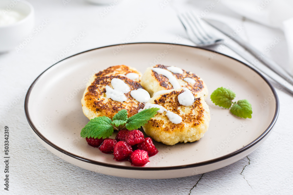 Cottage cheese pancakes with sour cream, raspberries and mint on a plate on the table.