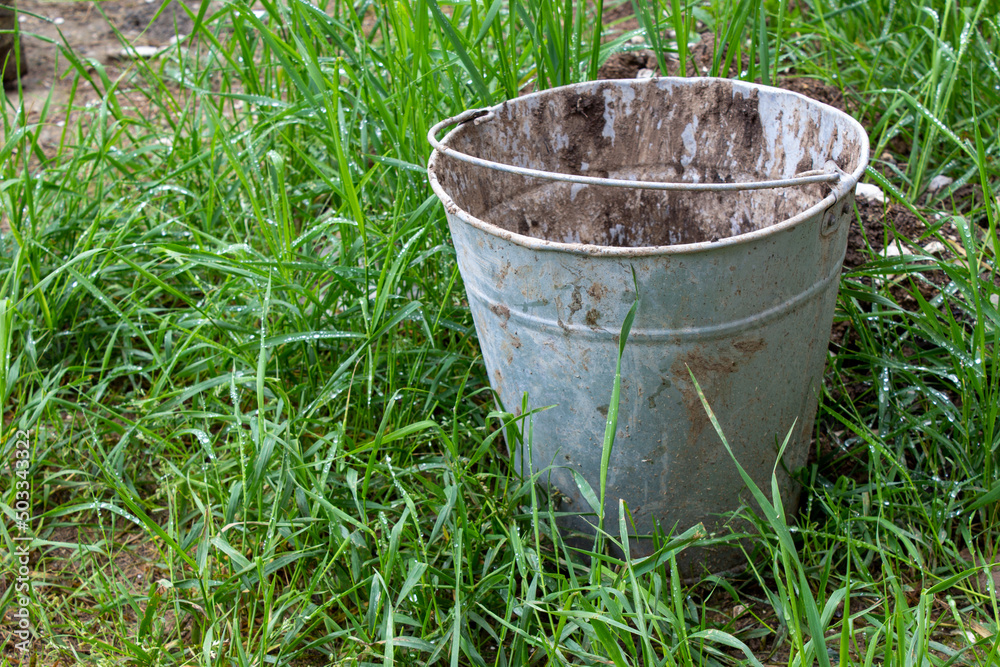 Old dirty bucket stained with paint on the street on the grass. Used metal bucket. Old dirty bucket stained with paint on the street on the grass. Used metal bucket.