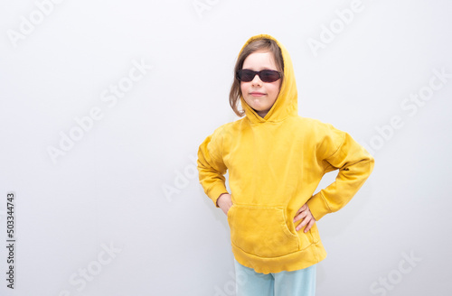 Child, Caucasian 6 years old, in a yellow sweatshirt with a hood on a gray background. Emotions on the face and hands on the hips
