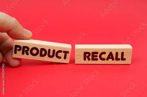 On a red background, wooden blocks, one of them in hand. The blocks are written - PRODUCT RECALL