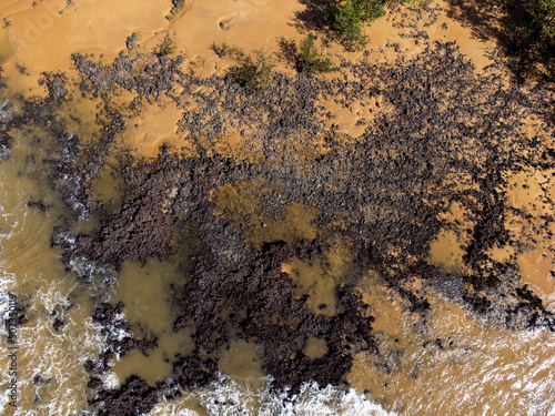 Beautiful beach with dark sands and black rocks like a volcano. Manguinhos, Espirito Santo, Brazil - aerial drone view photo