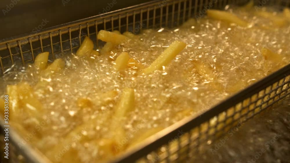 Close up of french fries is cooking into deep fryer. Crunchy potatoes is frying in hot boiling oil at cuisine. Process of making fast food at kitchen. Food preparing concept. Top view Slow motion Close up of french fries is cooking into deep fryer. Crunchy potatoes is frying in hot boiling oil at cuisine. Process of making fast food at kitchen. Food preparing concept. Top view Slow motion
