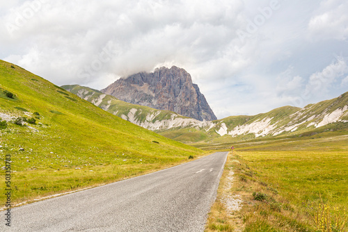 Empty road on the beautiful Apennine mountains in Abruzzo, Italy. Panoramic view of the Gran Sasso peak and the Campo Imperatore plateau with the road in perspective.
