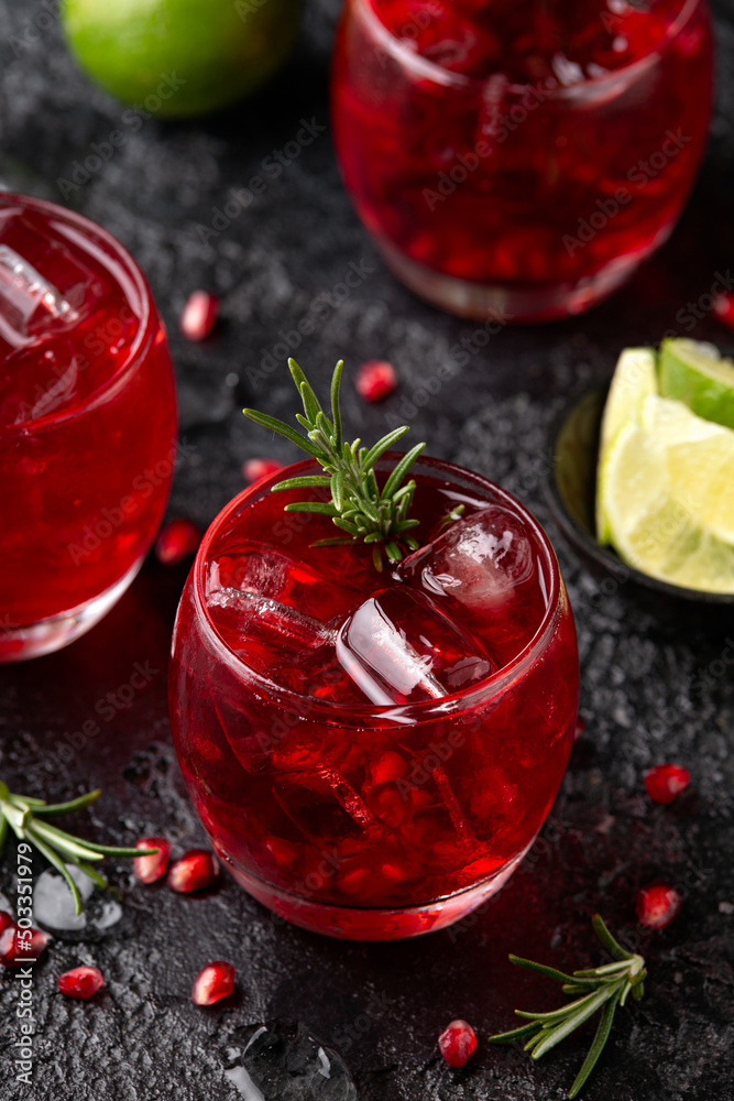 Pomegranate gin cocktail with lime, rosemary and ice on rustic black table Pomegranate gin cocktail with lime, rosemary and ice on rustic black table