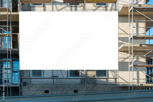 Blank white advertising banner mounted on the scaffoldings in front of the building under construction