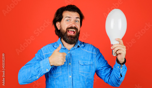 Good idea. Happy bearded man with light bulb shows thumb up. Male with lamp. Energy and electricity.