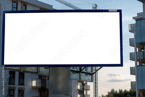 Blank white billboard for advertisement in front of the construction site. Residential ares with modern buildings on a sunny day