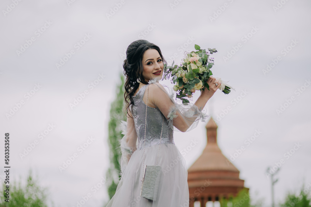 Elegant and smiling bridesmaid holding bridal bouquett in front of the church and posing for camera