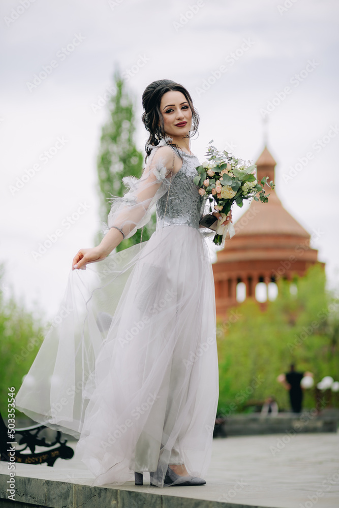 Young and pretty bridesmaid with bridal bouquet holding her elegant dress before the wedding ceremony