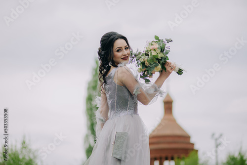 Obraz na płótnie Elegant and smiling bridesmaid holding bridal bouquett in front of the church and posing for camera w salonie