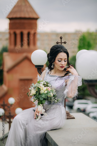 Very attractive bridesmaid sitting in front of the armenian apostolic church, holding bridal bouquet and posing for camera after the wedding ceremony