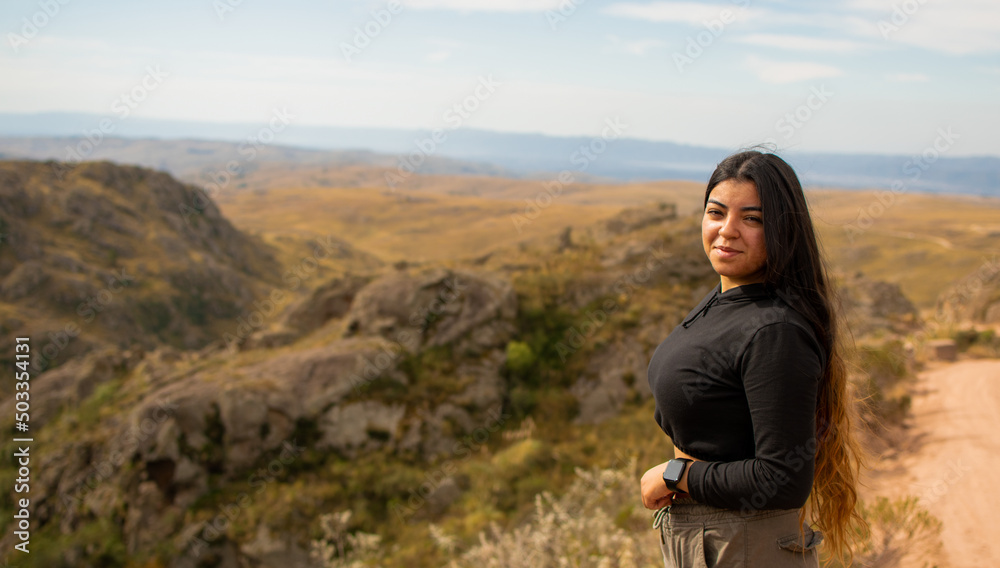 Portrait of Latin woman dressed in black with a cap having fun during the day of trekking in the mountain forest - looking at the camera