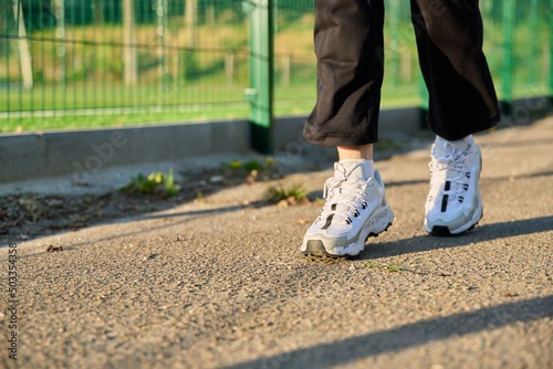 Close-up of female legs in white sneakers running along the road near the stadium