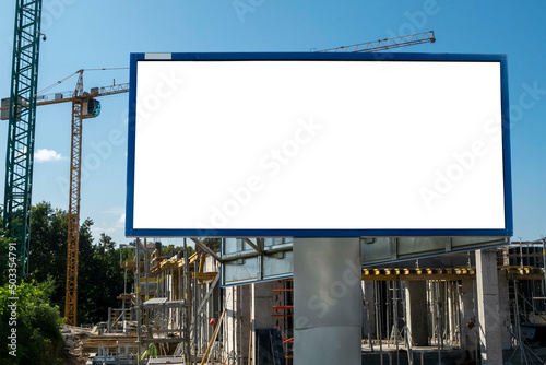 Blank white billboard for advertisement in front of the construction site on a sunny day