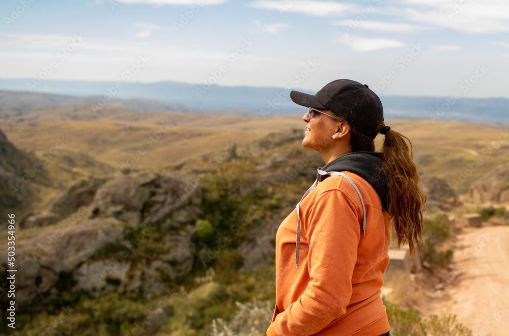 Portrait of latin woman dressed in orange with a cap and tail turned back having fun during the day of trekking in the mountain forest - looking at the horizon