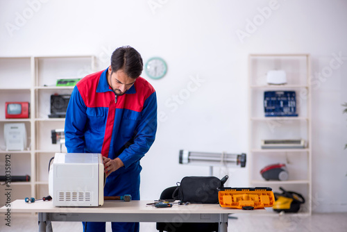 Young male repairman repairing oven at workshop