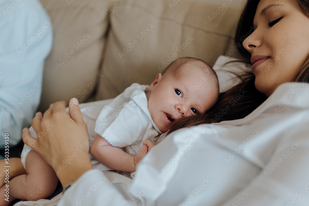 Newborn baby boy looking at the camera on top of his mother lying on the sofa Newborn baby boy looking at the camera on top of his mother lying on the sofa