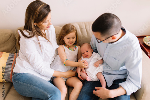 Happy family of four on the sofa with the newborn baby. Dad, mom, daughter and son