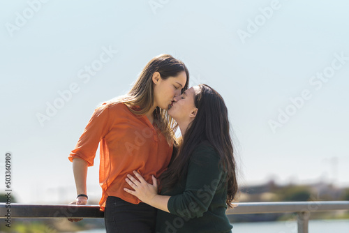 lesbian couple kissing while one of them is climbing on a railing