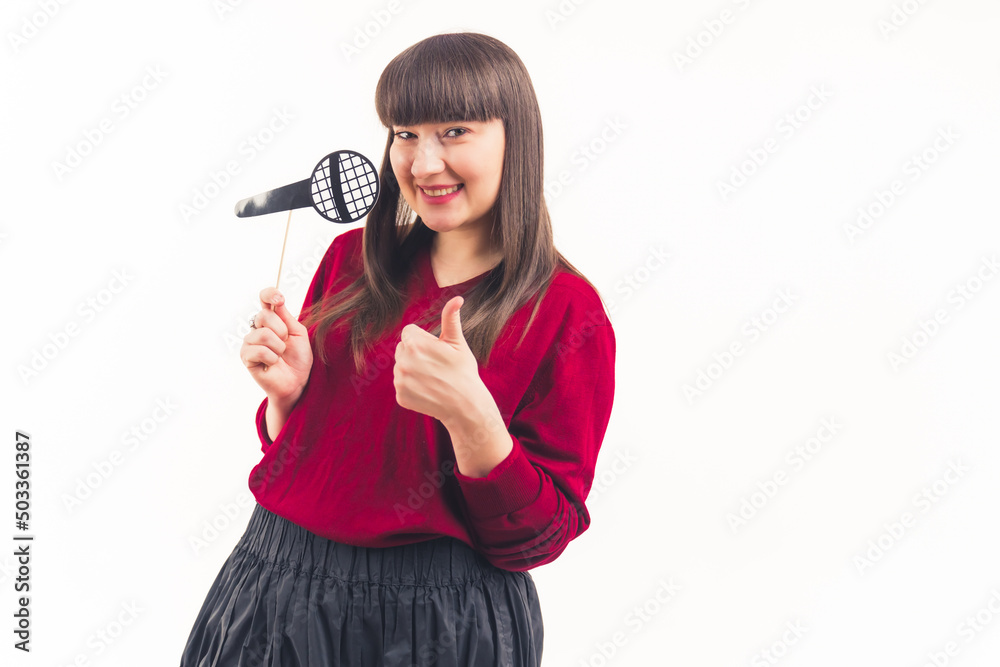 young woman with dark straight hair having fake props microphone on a stick and showing thumb up white background isolated copy space studio shot . High quality photo young woman with dark straight hair having fake props microphone on a stick and showing thumb up white background isolated copy space studio shot . High quality photo