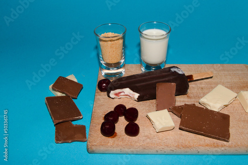 chocolate ice cream on a wooden board with cubes of black and white chocolate cherries milk on a blue background