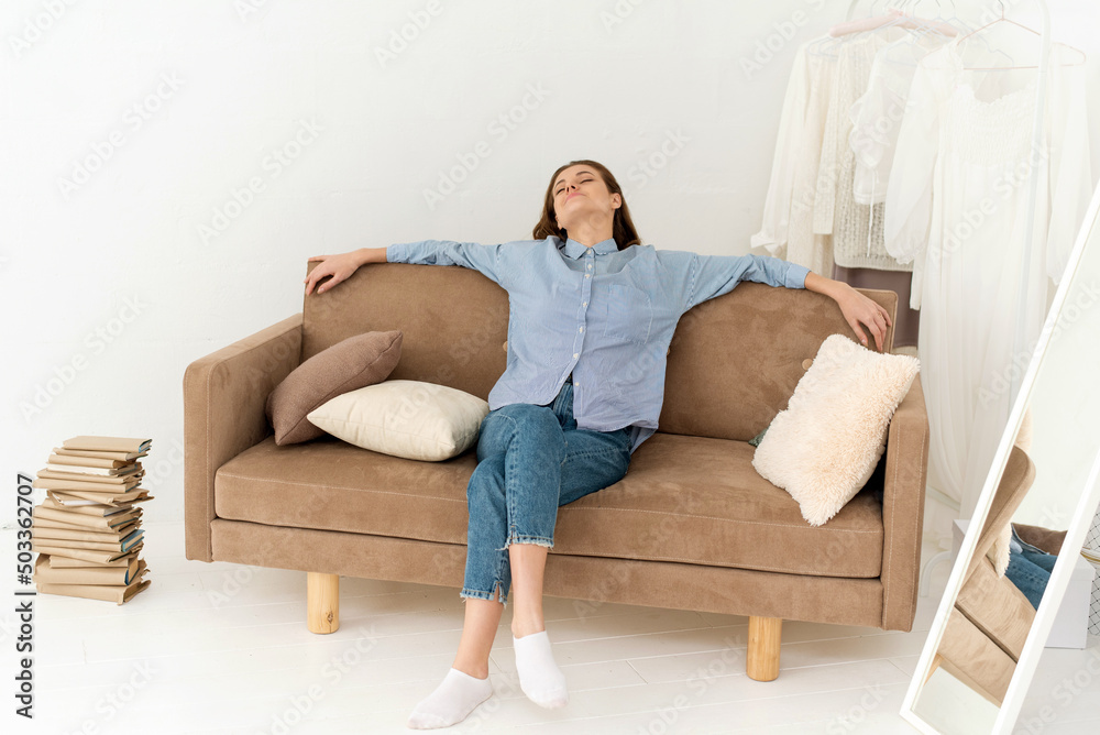 Calm young woman resting on a soft comfortable sofa, sitting enjoying a carefree peaceful morning, relaxing on the sofa