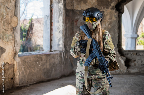 Portrait of a woman in a helmet and goggles with a machine gun in her hands. A female soldier in a camouflage uniform holds a weapon.